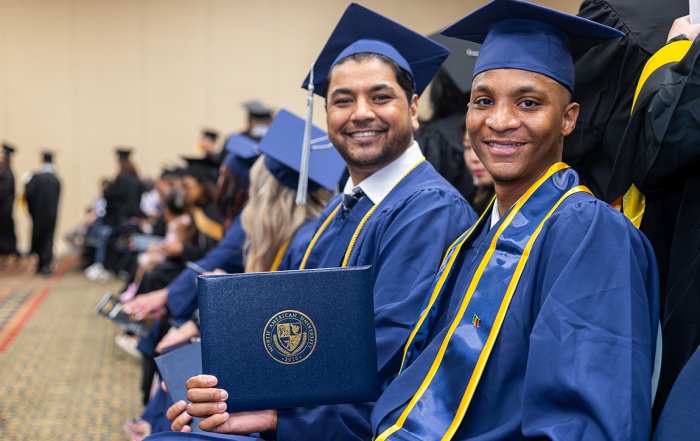 Two NAU students smiling with a diploma at commencement